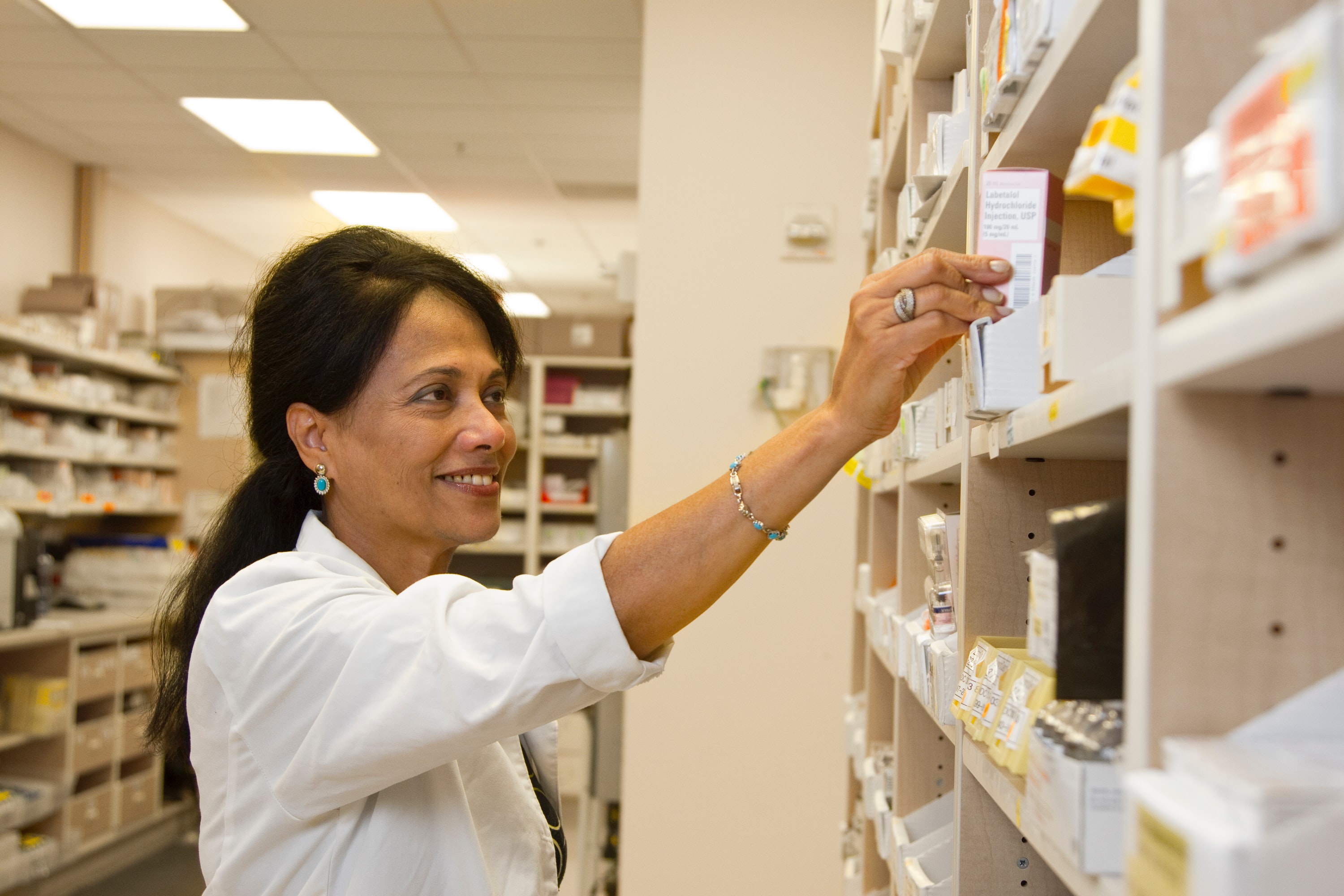 A pharmacist in one of the legit online pharmacies pulls a dispensing box of medication from a shelf.