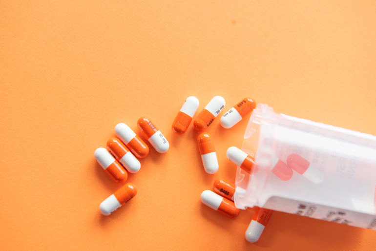 A prescription bottle and capsules against an orange background