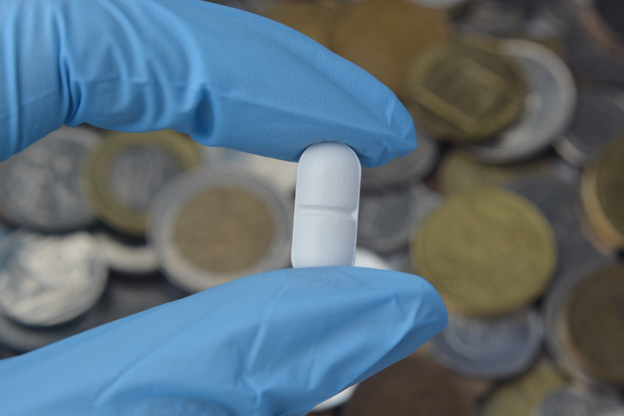 Holding a pill with two fingers over a pile of coins