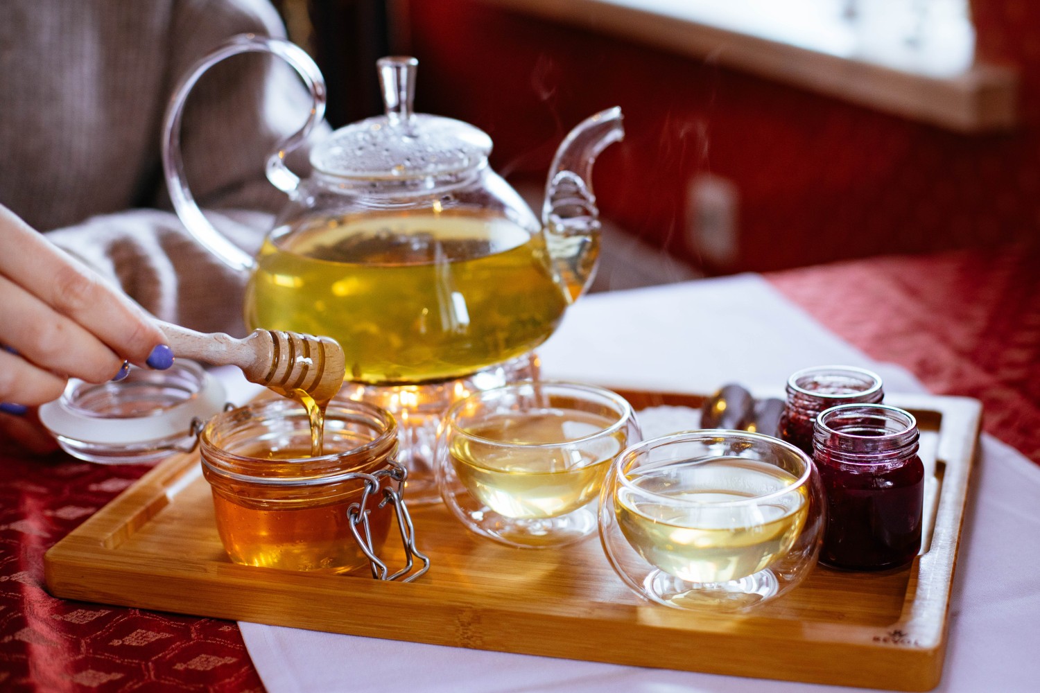 A person holding a honey stick next to a teapot